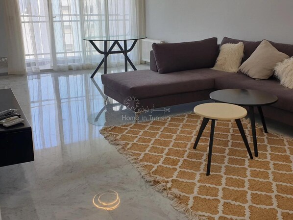 Un salon moderne avec un canapé marron foncé, une table basse ronde et une table avec un plateau en verre.