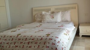A neatly made bed with floral bedding, a white headboard with a grid pattern, and a bedside table with a drawer. - Lovely, apparently feet in the water (sousse)
