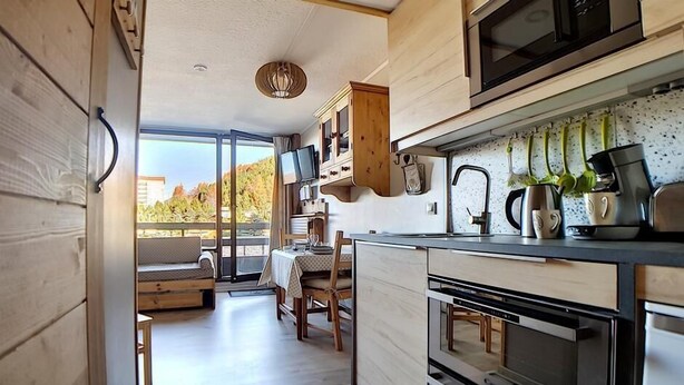 Een moderne keuken met houten kastjes, een inbouwoven en een eethoek met een tafel en stoelen.
