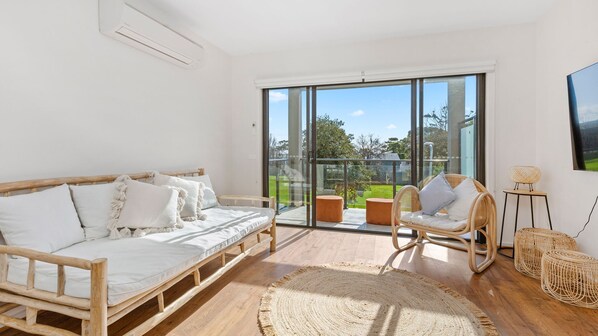 A modern bedroom with a wooden bed, a wicker chair, and a large sliding glass door leading to a balcony. - OSPREY - MORNINGTON. Walking distance to Mornington's cafe culture. (Mornington)