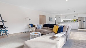 Una sala de estar moderna con sofá, mesa de centro y comedor, con cocina al fondo.