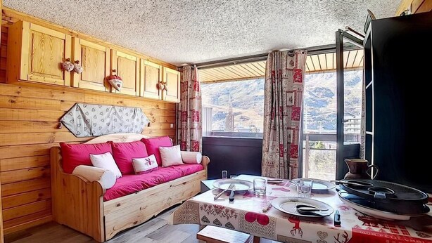 A cozy room with a wooden sofa, a dining table with plates and glasses, and a view of mountains through the window. - Ski-in/ski-out & foot of the slopes, 2nd floor, balcony, tv, 20m², Les Menuires (Les Menuires)