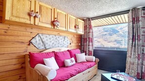 A wooden cabin with a sofa, a small table, and a window with curtains. - Ski-in/ski-out & foot of the slopes, 2nd floor, balcony, tv, 20m², Les Menuires (Les Menuires)