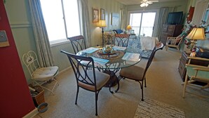 Un coin repas avec une table en verre entourée de chaises, un téléviseur posé sur un meuble et un ventilateur de plafond.