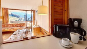 Una cocina acogedora con cafetera, una mesa lista para dos personas y vistas a la montaña a través del ventanal.