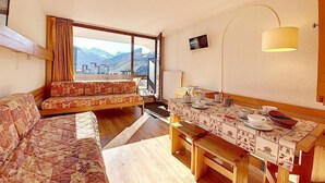 Una habitación acogedora con sofá, una mesa de comedor con vajilla, televisor y ventana con vistas a la montaña.