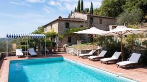 A pool area with lounge chairs and umbrellas, a stone building in the background, and a clear sky.