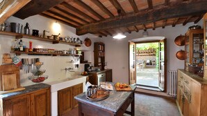 A rustic kitchen with wooden beams, a stone floor, and a view to an outdoor patio.