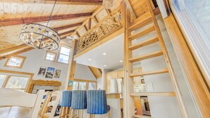 A wooden interior with a high ceiling, a chandelier, and a kitchen area.
