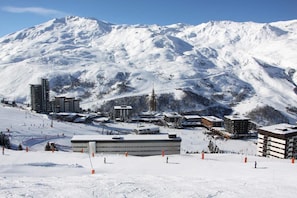 Estância de esqui coberta por neve, com edifícios modernos, pistas e montanhas ao fundo.