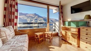 A cozy room with a large window, wooden furniture, and a flat-screen TV. - 100m from ski slopes, 7th floor, view mountain, balcony, tv, ski locker, 36m², Les Menuires (Les Menuires)