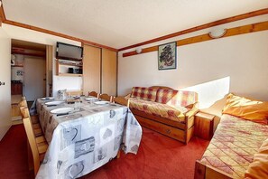 Una camera compatta con un tavolo da pranzo apparecchiato per quattro persone, un divano, un letto e una piccola credenza in legno.
