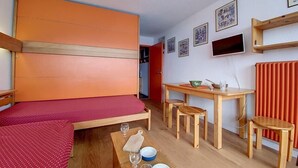 A compact room with a bed, a small dining table, and a red curtain. - 100m from ski slopes, 5th floor, view ski slopes, balcony, tv, ski locker, 24m², Les Menuires (Les Menuires)