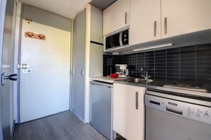 Una cocina compacta con armarios blancos, microondas, cafetera y lavavajillas.