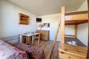 A compact room with a bunk bed, a desk with a chair, a dresser, a television mounted on the wall, and a small table with cups. - At the foot of shops, 6th floor, balcony, tv, ski locker, 17m², Les Menuires (Les Menuires)