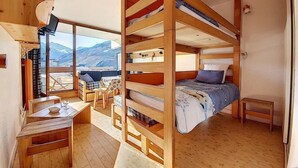 Una cabaña acogedora con literas, muebles de madera, un comedor y un amplio ventanal con vistas a la montaña.