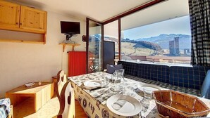 Un comedor con una mesa lista para cuatro, un televisor montado en la pared y vistas a un paisaje montañoso a través de amplios ventanales.