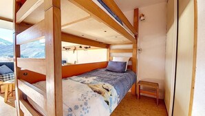 Habitación con literas, techo de madera, una pequeña mesa y vistas a las montañas.