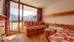 A hotel room with a wooden bed, a sofa, a small table, and a view of mountains through a large window. - 100m from ski slopes, 2nd floor, balcony, tv, ski locker, 24m², Les Menuires (Les Menuires)