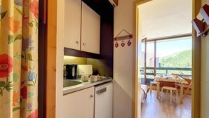 A compact kitchen with a sink, stove, and a small refrigerator. A dining area with a table and chairs is visible through an open door. - At the foot of shops, 5th floor, view valley, balcony, tv, ski locker, 17m², Les Menuires (Les Menuires)