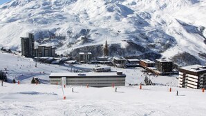 A snow-covered ski resort with modern buildings, ski slopes, and a mountain backdrop. - At the foot of shops, 5th floor, view valley, balcony, tv, ski locker, 17m², Les Menuires (Les Menuires)