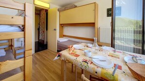 A compact room with bunk beds, a dining table set for two, and a sliding glass door leading to a balcony. - At the foot of shops, 5th floor, view valley, balcony, tv, ski locker, 17m², Les Menuires (Les Menuires)