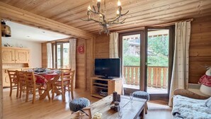 L’intérieur d’un chalet en bois comprend un coin repas, un téléviseur et un balcon.