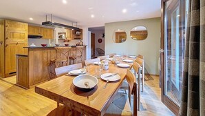Une cuisine moderne avec des meubles en bois, une table à manger dressée pour six personnes et une grande fenêtre avec des rideaux.