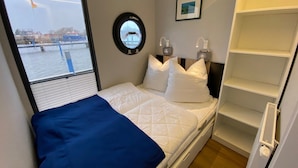 A bedroom with a bed, a window, a bedside table, a mirror, and a shelf.