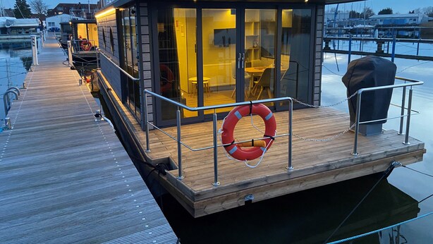A modern boat with a glass-enclosed dining area, a lifebuoy, and a covered grill.