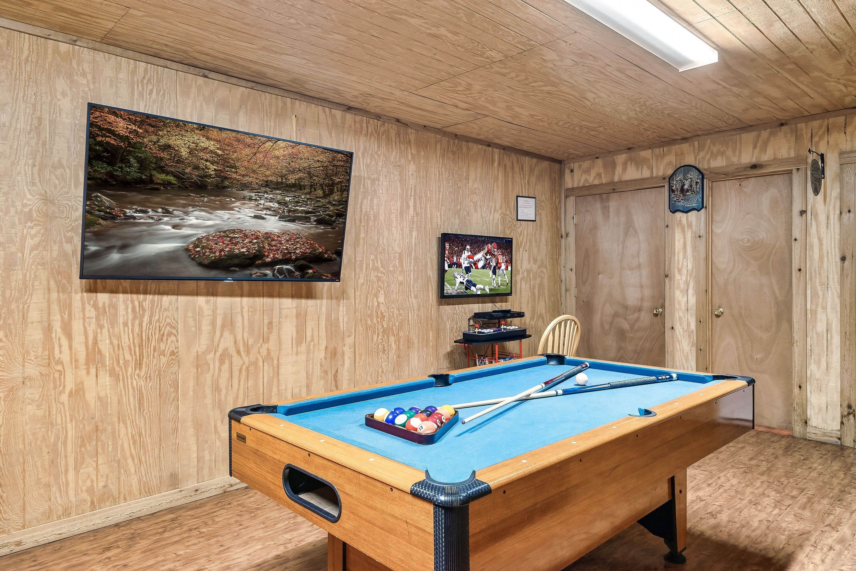 A pool table with balls, a framed photograph, and a wooden wall with a framed picture.
