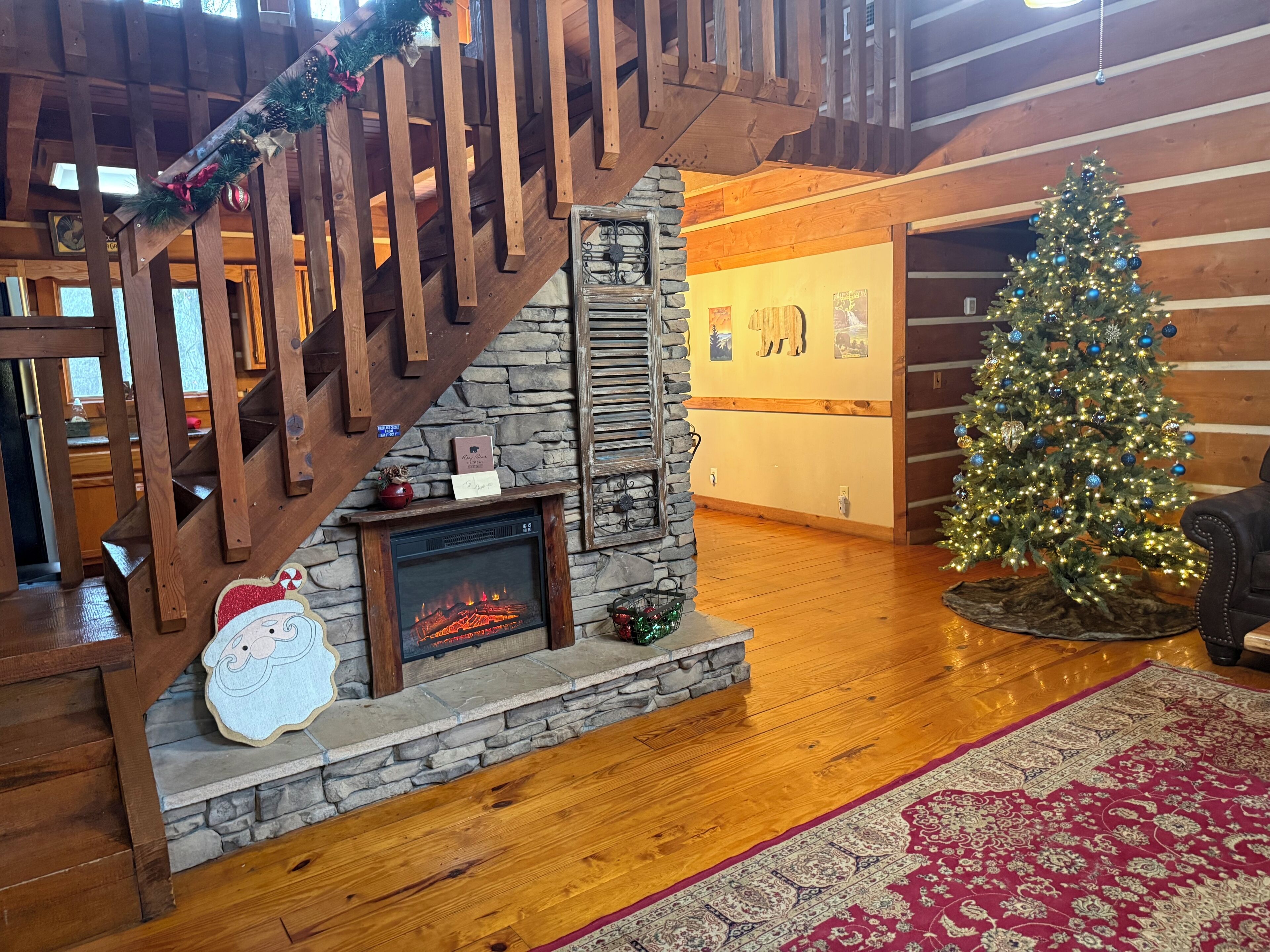 Un interior acogedor con chimenea, escalera de madera y un árbol de Navidad decorado.