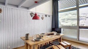A dining area with a wooden table set for four, a red pendant light, and heart-shaped decorations on the wall. - 200m from resort center, 12nd floor, balcony, tv, ski locker, 37m², Les Menuires (Les Menuires)