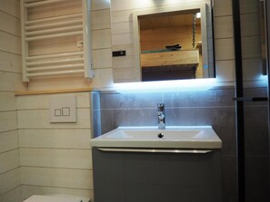 Une salle de bain avec un lavabo blanc, un miroir au-dessus et une étagère en bois.