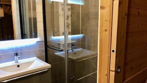 Kylpyhuone, jossa on lasiseinäinen suihkukaappi, valkoinen pesuallas ja puuovi.