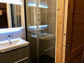 A bathroom with a glass shower enclosure, a white sink, and a wooden door. - 50m from ski slopes, Ground floor, balcony, tv, ski locker, 19m², Les Menuires (Les Menuires)