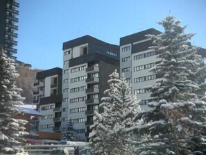 Un immeuble à plusieurs étages doté de balcons, entouré d’arbres couverts de neige.