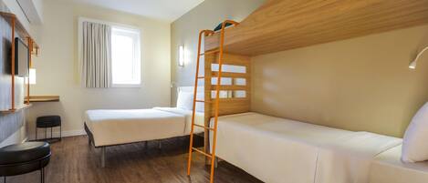 A hotel room with a bunk bed, a desk with a chair, a window with curtains, and a wooden floor.