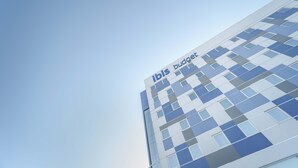 Een modern gebouw met een glazen gevel en de tekst ‘ibis budget’ op de zijkant.