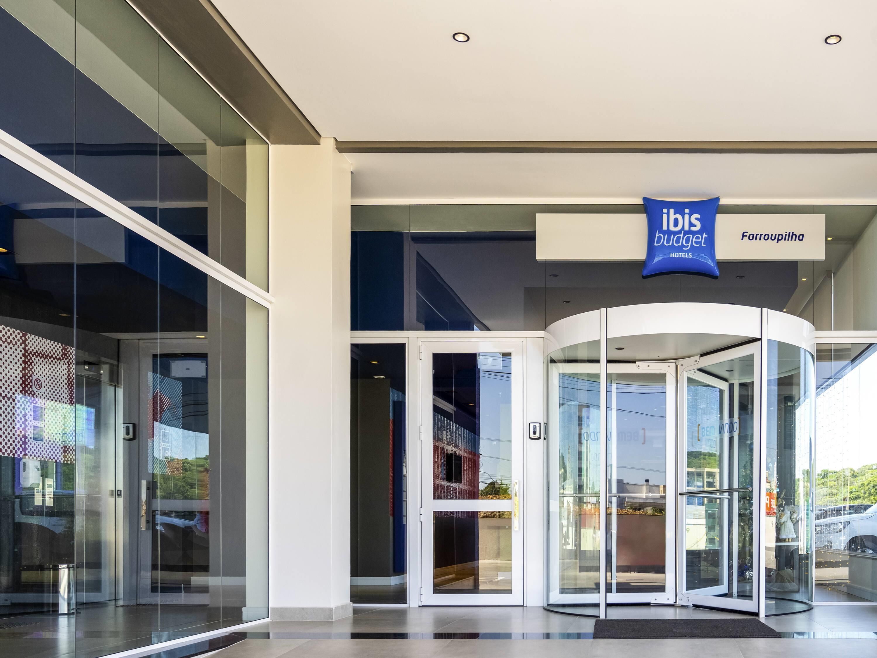 Entrada de hotel con puerta giratoria, puertas de vidrio y cartel anunciando ibis budget hotels.
