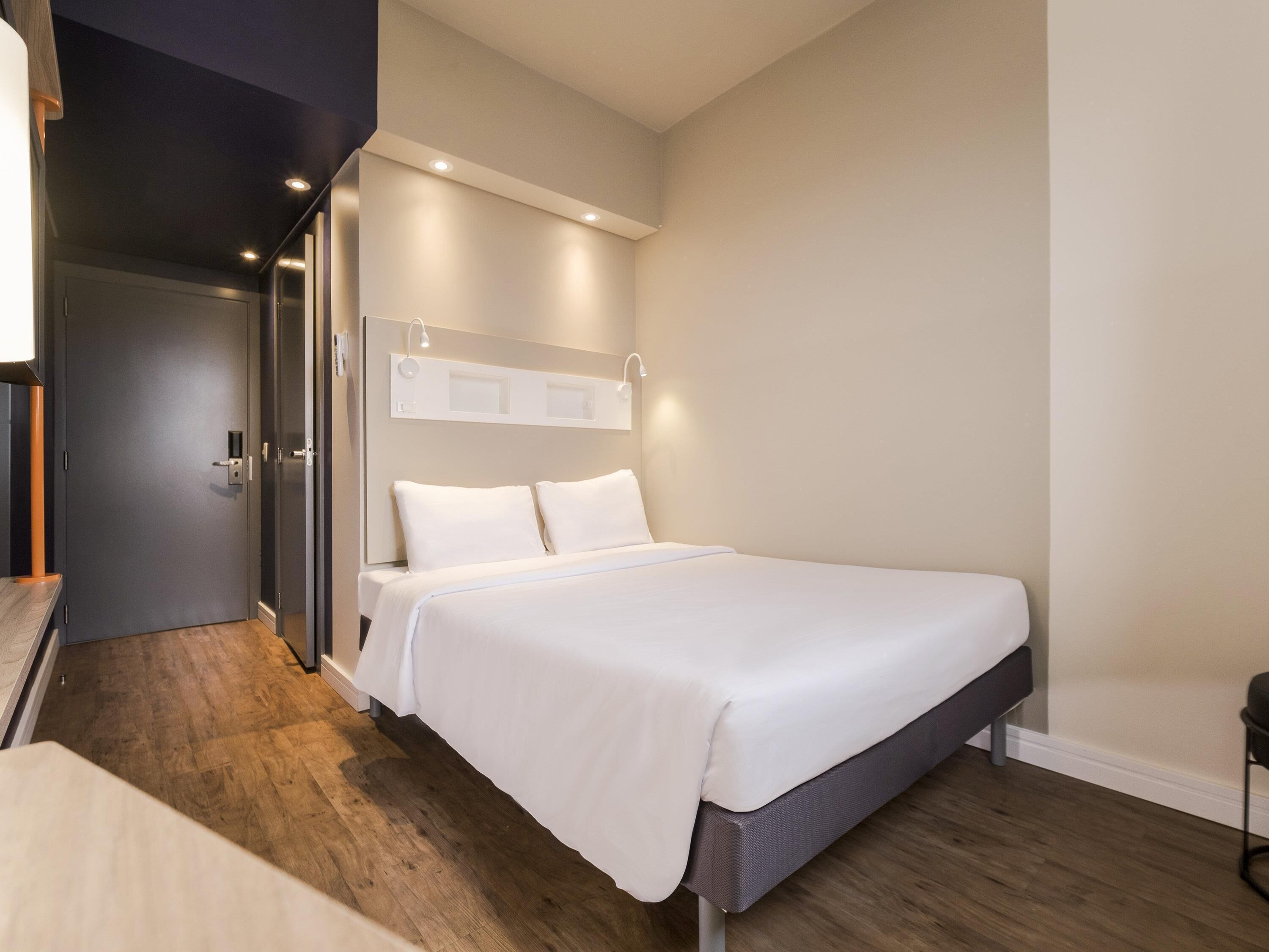 Una habitación de hotel moderna con una cama, una mesita de noche, un armario y una puerta.
