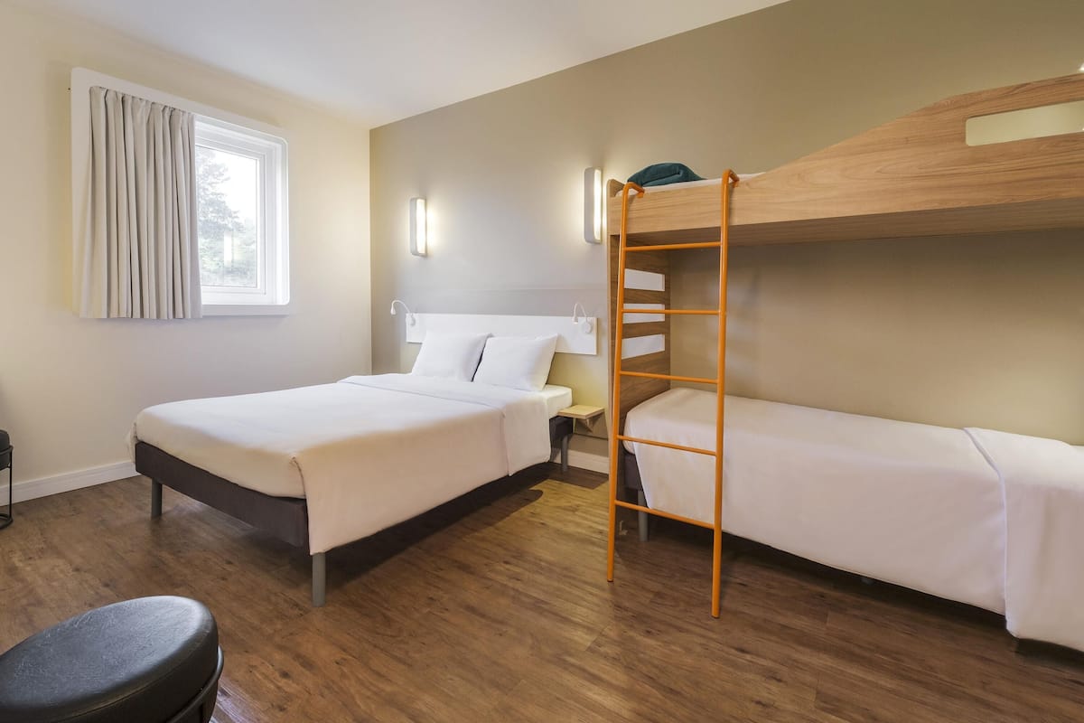 Ein Zimmer mit Etagenbett, einem Einzelbett, einem Schreibtisch, einem Stuhl, einem Vorhangfenster und Wandleuchten.