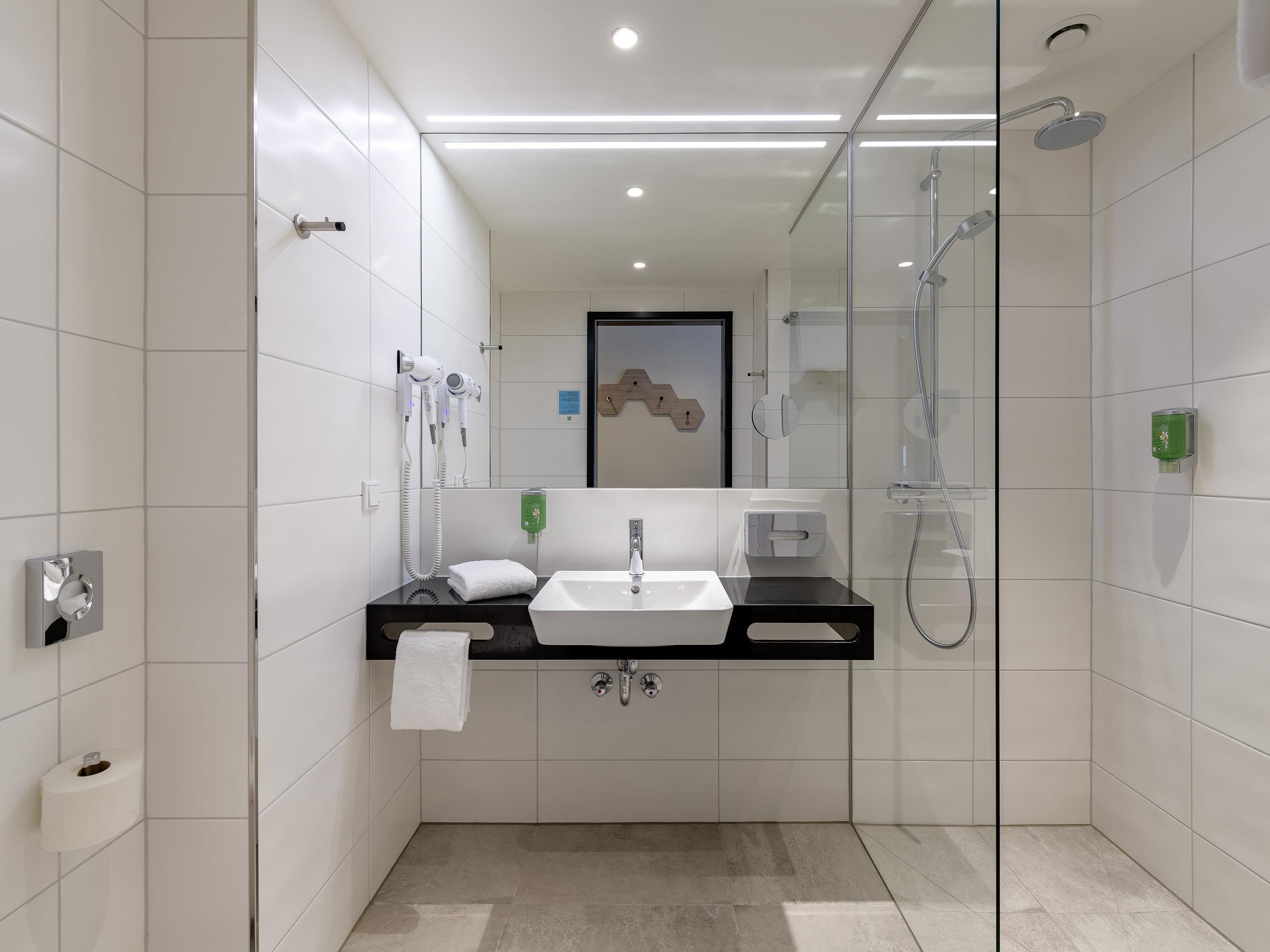 Une salle de bain moderne avec une douche à parois de verre, un lavabo blanc et un sèche-cheveux fixé au mur.