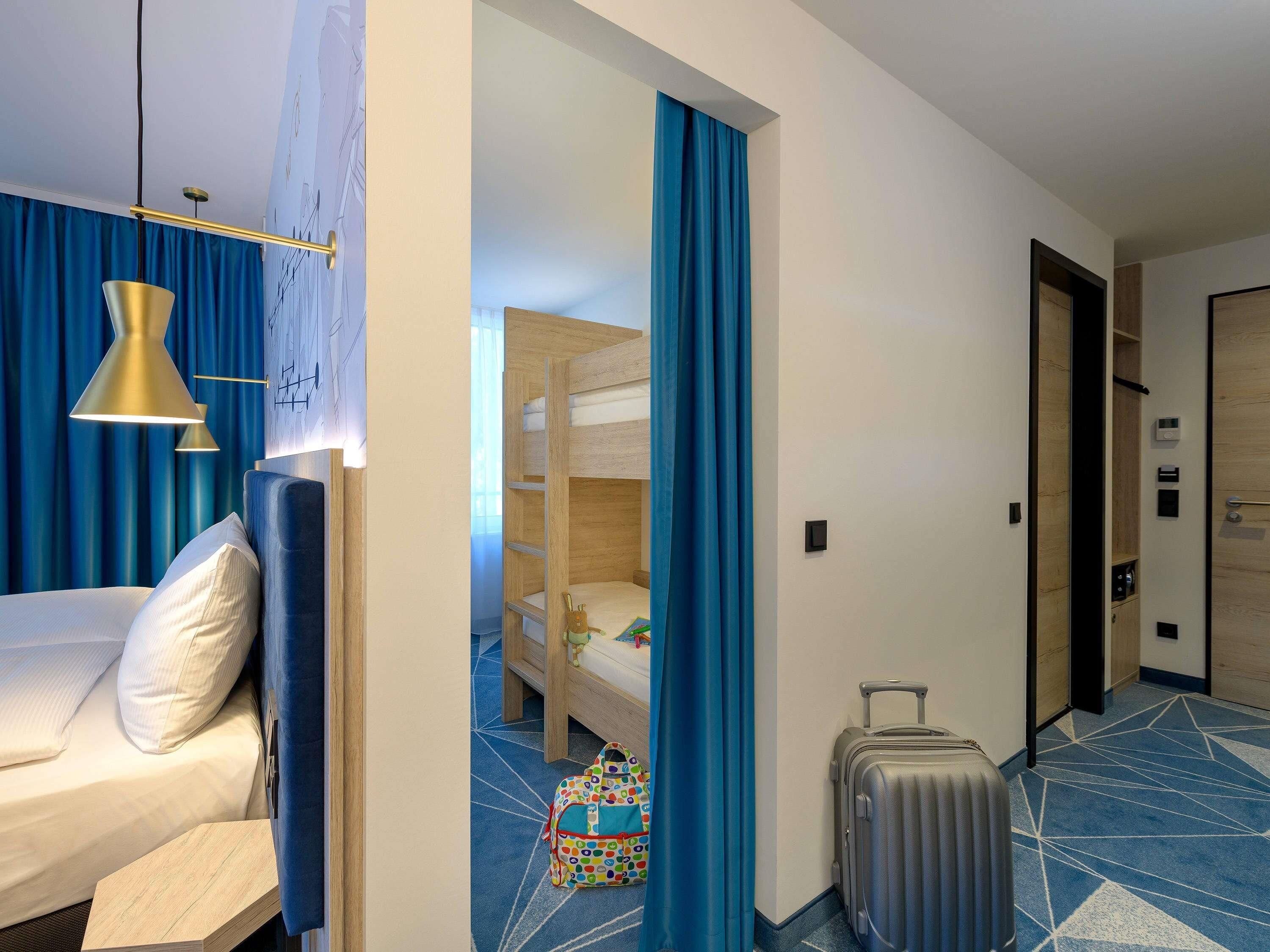 A hotel room with a bed, a desk, a chair, a suitcase, and a bathroom visible through an open door.