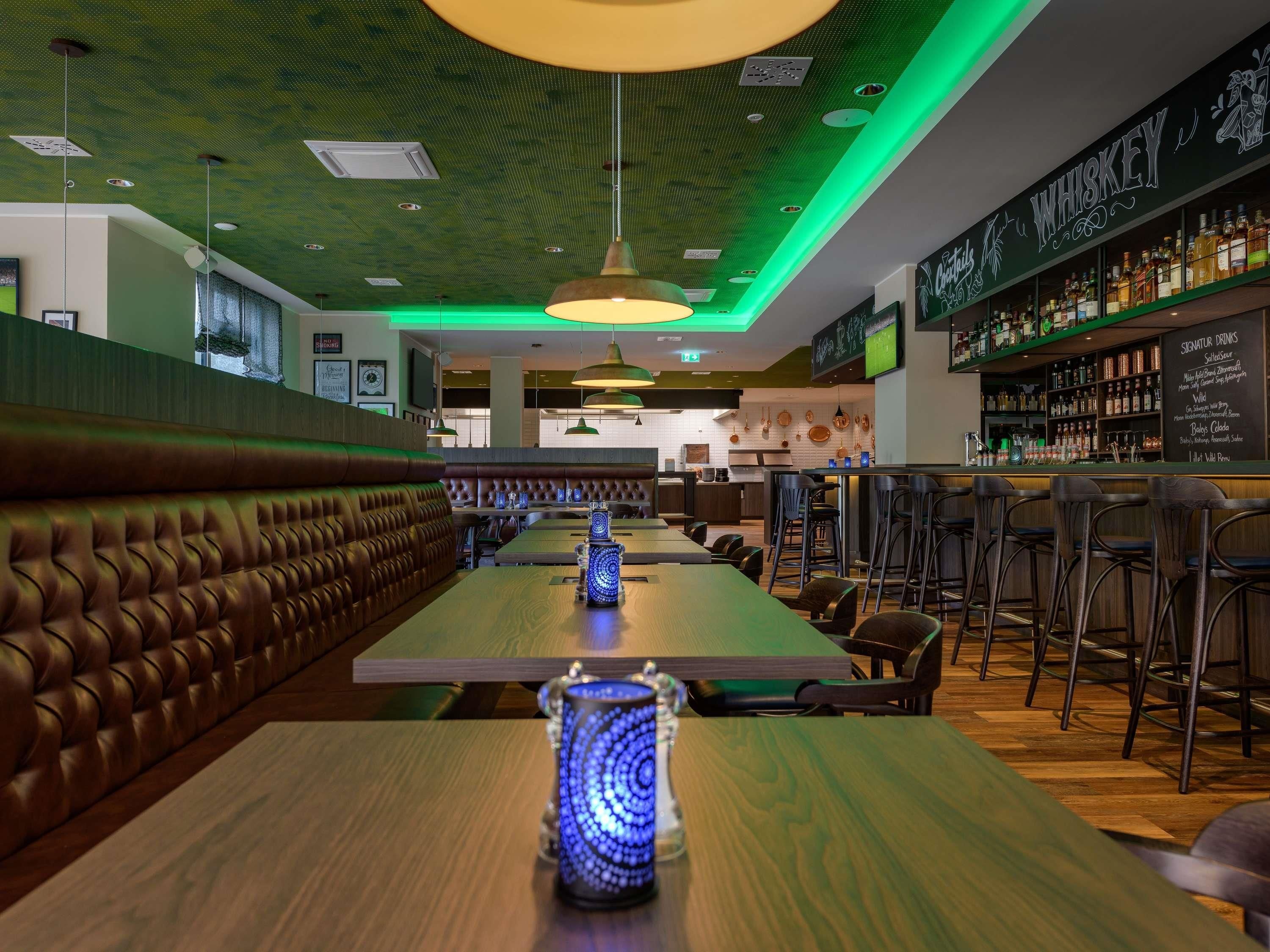 A restaurant interior with a long wooden bar, leather booth seating, hanging pendant lights, and a bar area with shelves of bottles.