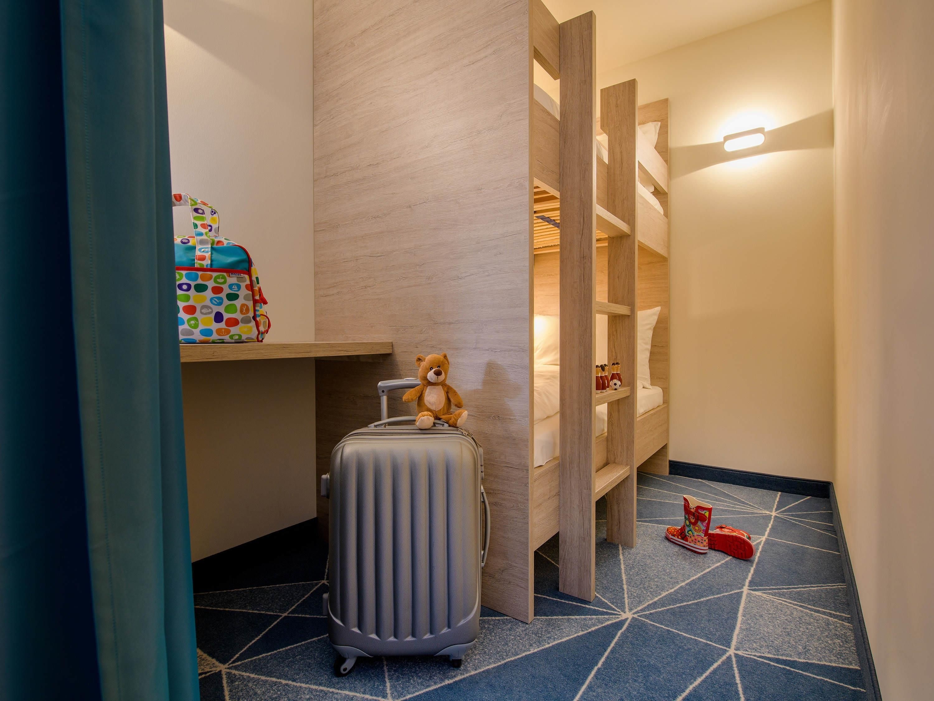 Ein Hotelzimmer mit Koffer, Teddybär und Kinderrucksack auf einem Regal.