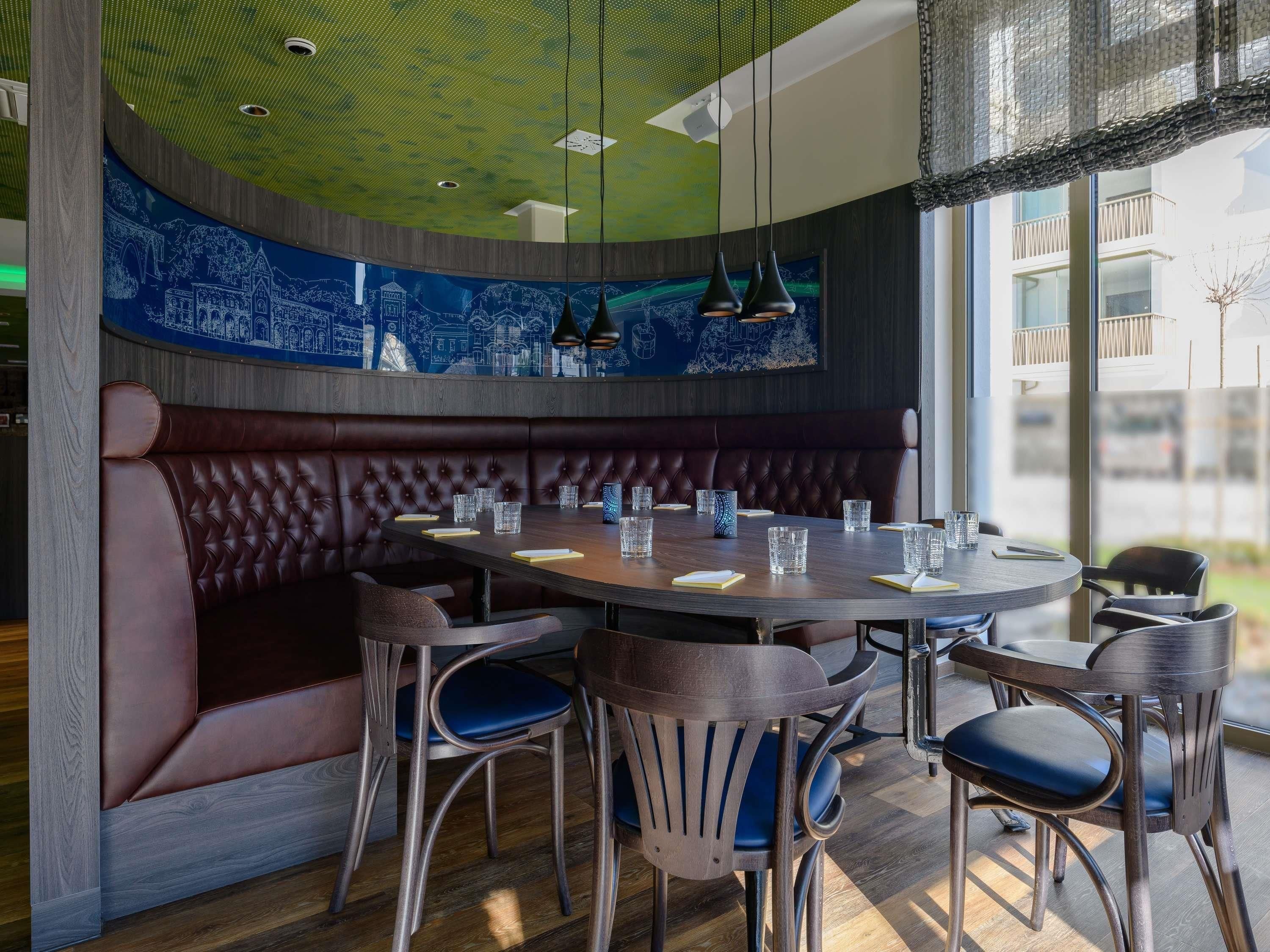 Un restaurante con una mesa redonda, asientos tipo banca en tono marrón oscuro y sillas azules.