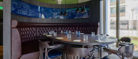 Un restaurante con una mesa redonda, asientos tipo banca en tono marrón oscuro y sillas azules.