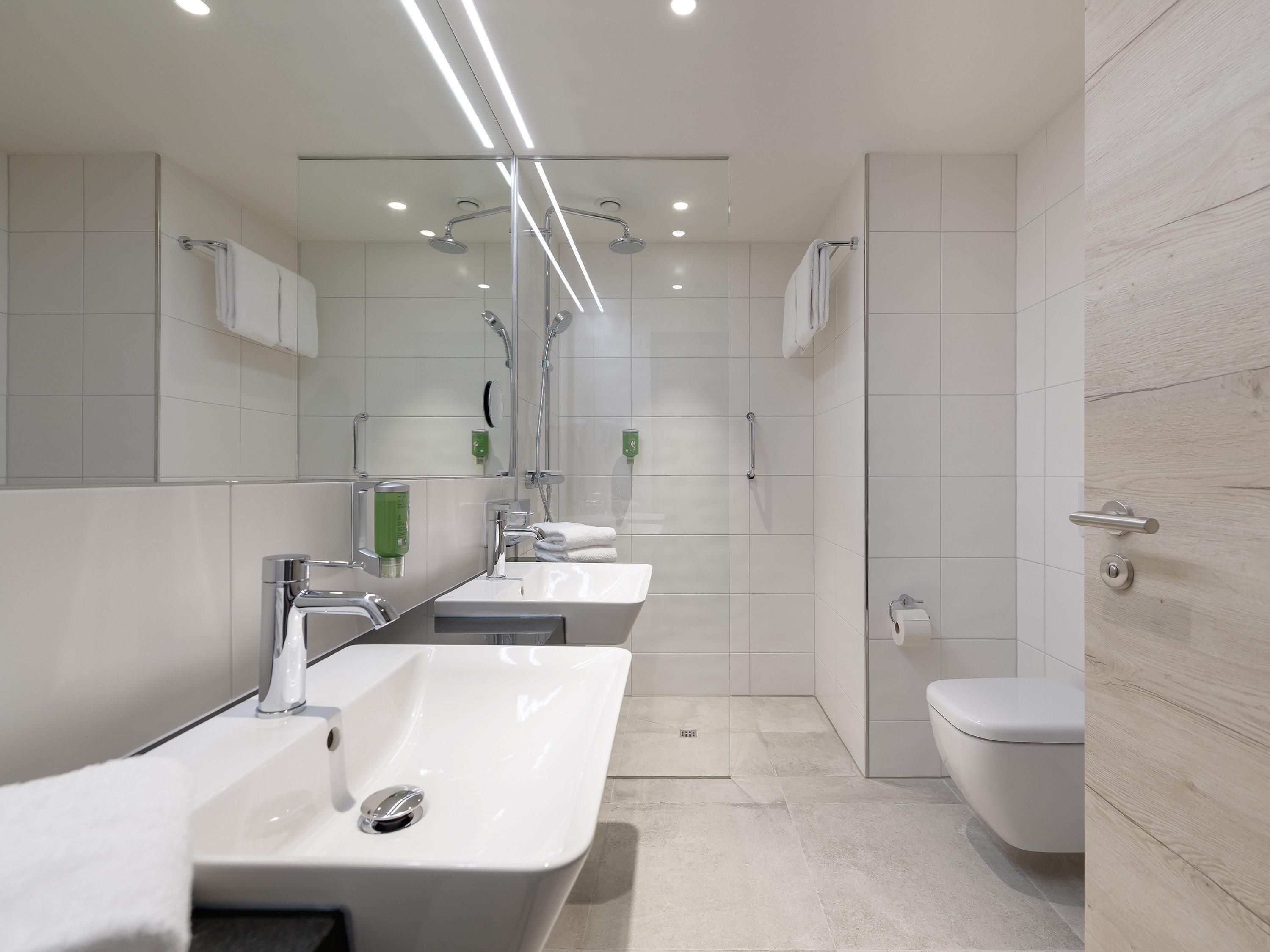 Et moderne badeværelse med et stort spejl, vask, toilet og bruseområde.