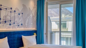 A hotel room with a large bed, a headboard with a geometric design, and a view of a mountain through a sliding glass door. - ibis Styles Bad Reichenhall (Bad Reichenhall)